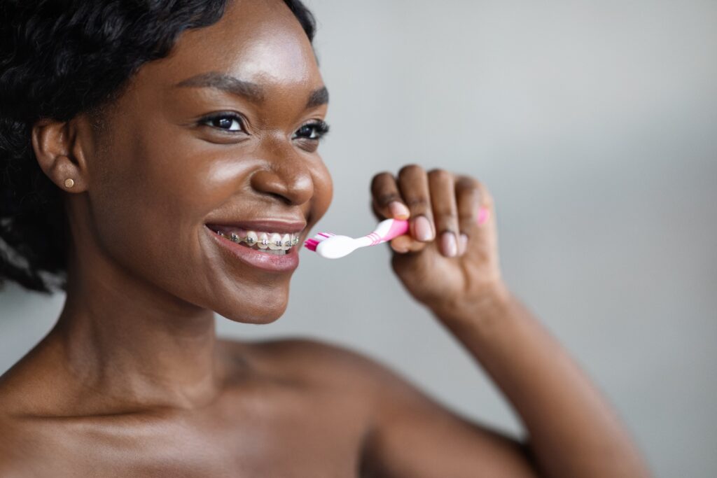 Woman with braces smiling while brushing her teeth